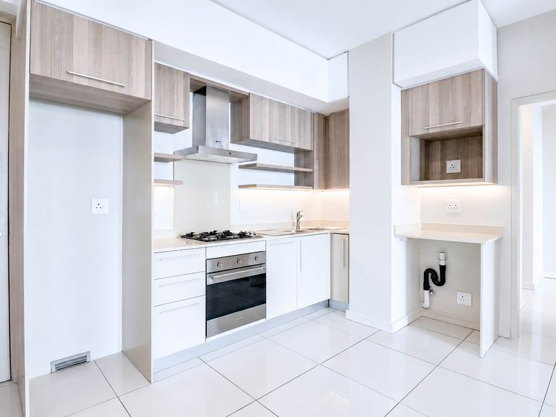 Modern kitchen featuring sleek wood-tone and white cabinetry, stone countertops, integrated gas hob, electric oven, and high-quality tiled flooring.