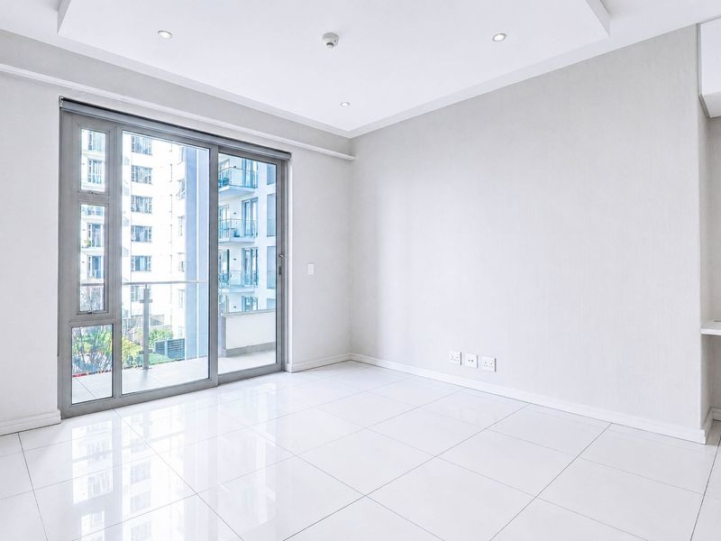 A bright, modern, and empty living area featuring polished porcelain floor tiles, recessed ceiling lighting, and a sliding glass door leading to a balcony.