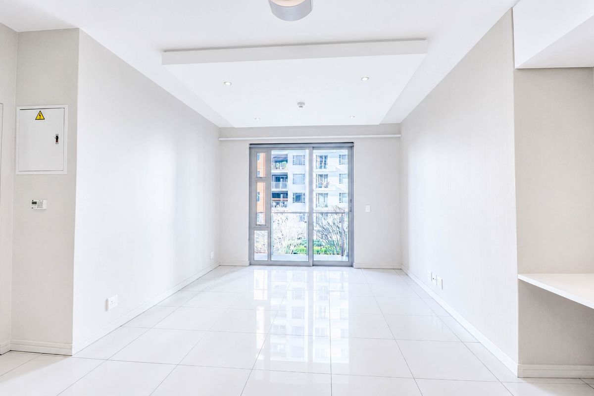 A bright, empty living room featuring modern tiled flooring, a recessed ceiling with downlights, and a sliding glass door leading to a balcony.