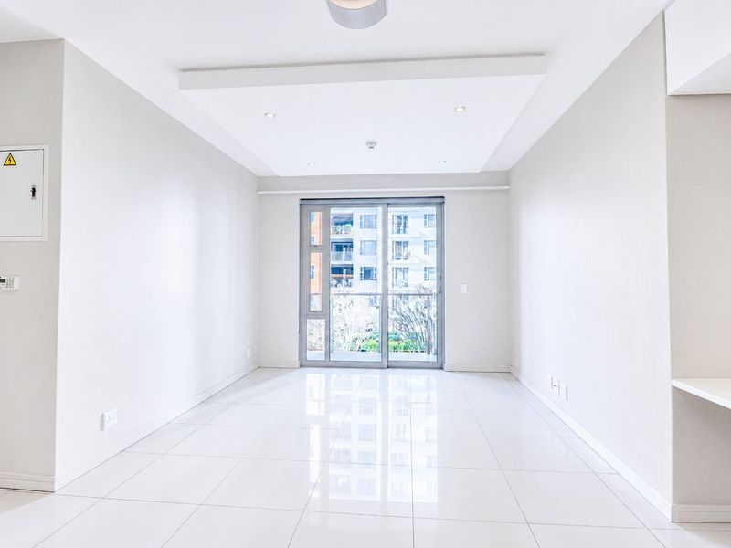 A bright, empty living room featuring modern tiled flooring, a recessed ceiling with downlights, and a sliding glass door leading to a balcony.