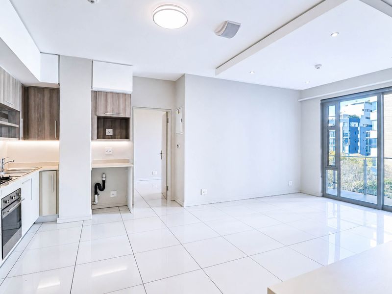 Modern open-plan kitchen and living area featuring sleek cabinetry, integrated appliances, high-gloss tiled floors, and large sliding doors leading to a balcony.