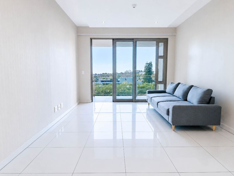 Bright and modern living area featuring polished tiled floors, recessed lighting, and large sliding glass doors leading to a private balcony with scenic views.