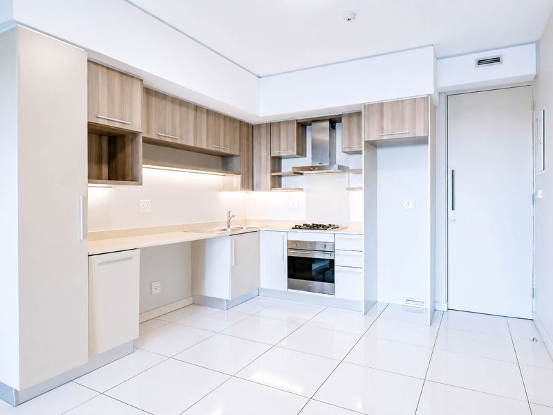 Modern kitchen featuring sleek wood-tone cabinetry, stone countertops, integrated stainless steel appliances, and polished white floor tiles in a clean, minimalist layout.