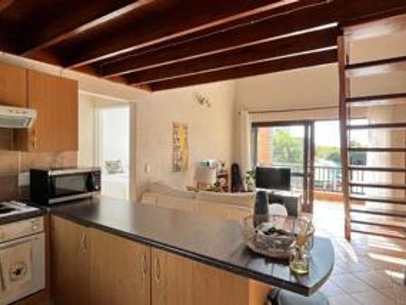 Open-plan living area featuring a kitchen with laminate cabinetry, exposed timber ceiling beams, and a timber staircase leading to an upper level.