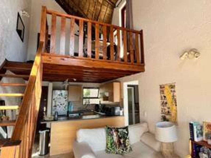 Open plan living area featuring a mezzanine level with wooden staircase and balustrade, overlooking a compact kitchen with built-in cabinetry.