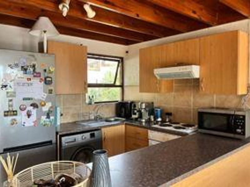 Functional kitchen featuring laminate cabinetry, tiled backsplash, electric hob, extractor fan, and exposed timber ceiling beams.