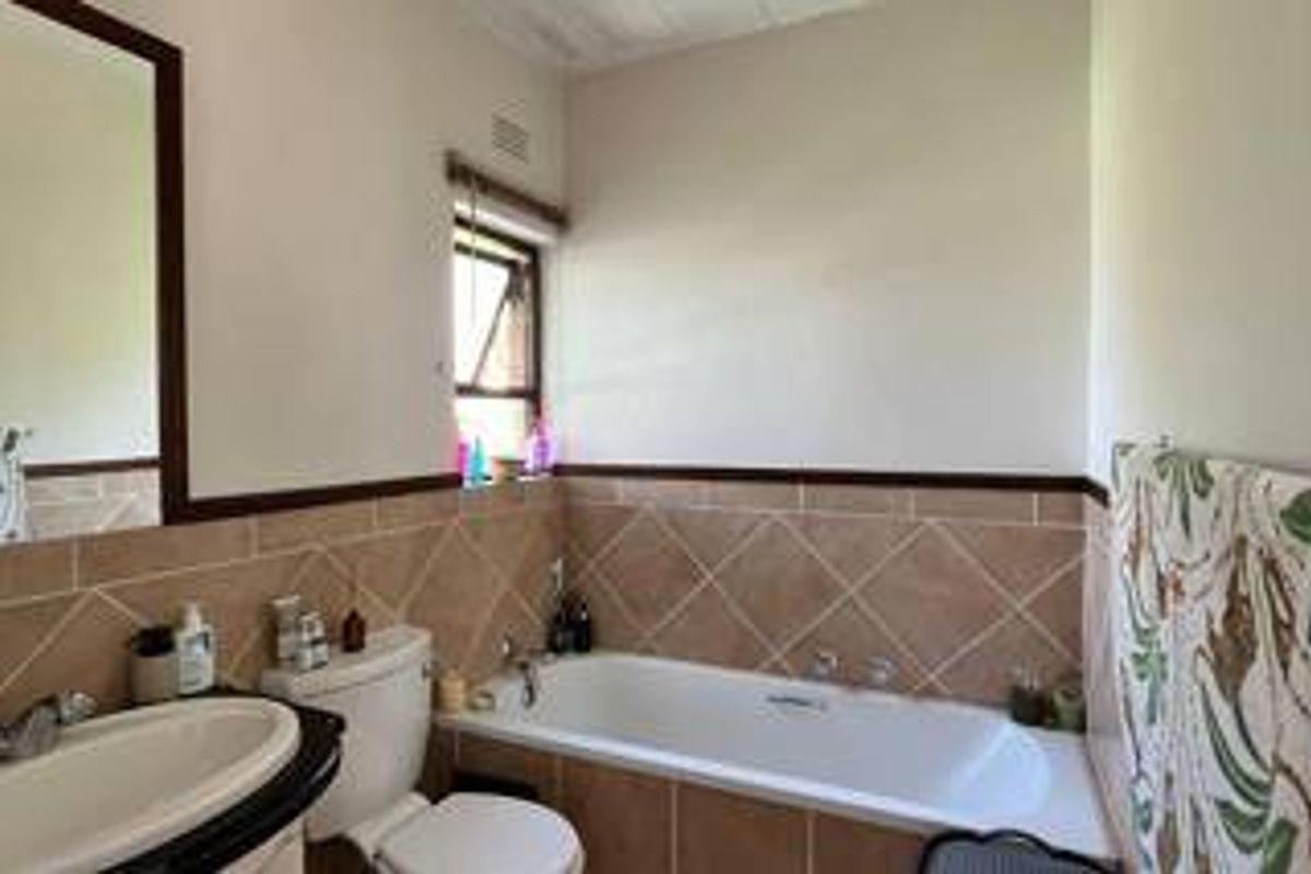 A functional bathroom featuring a built-in bathtub, tiled splashback, vanity basin, and wall-mounted mirror.