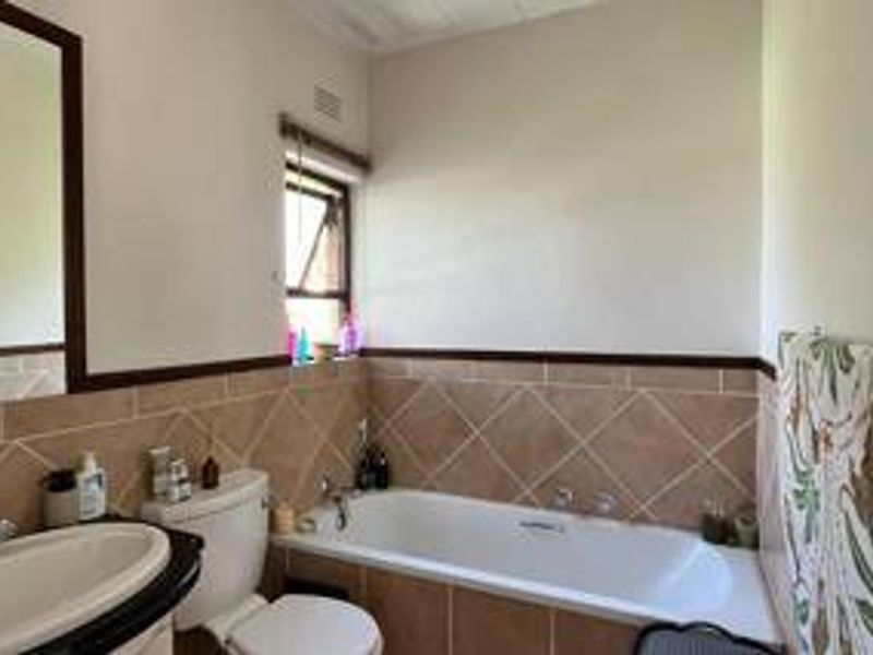 A functional bathroom featuring a built-in bathtub, tiled splashback, vanity basin, and wall-mounted mirror.