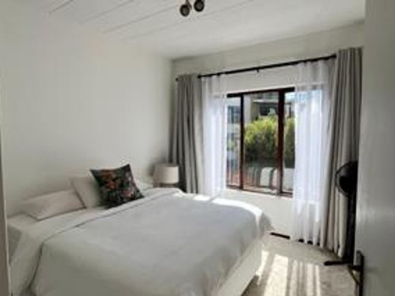 A well-lit bedroom featuring a large window with curtain tracks and a simple ceiling-mounted spotlight fixture.