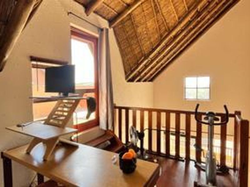 A loft-style office space featuring a high thatched ceiling with exposed timber rafters, wooden flooring, and a timber balustrade overlooking the lower level.
