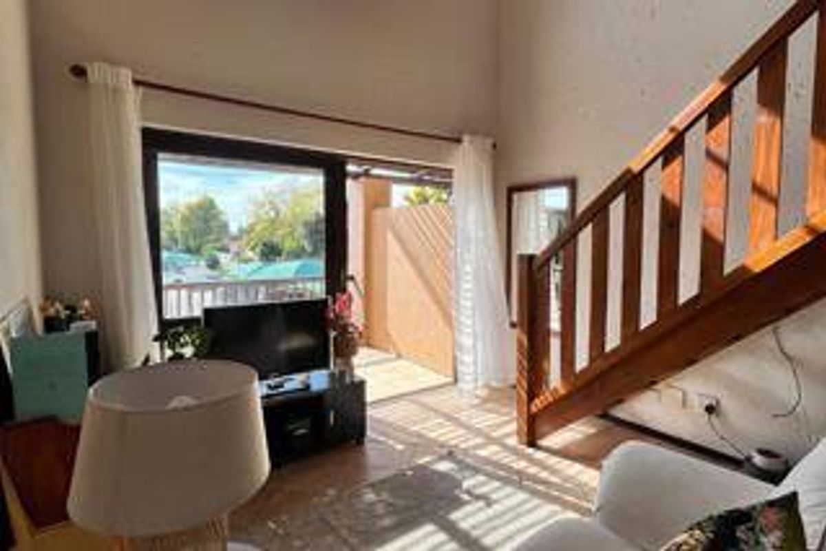 A bright living room featuring a wooden staircase, high ceilings, and sliding glass doors that open onto a private balcony.