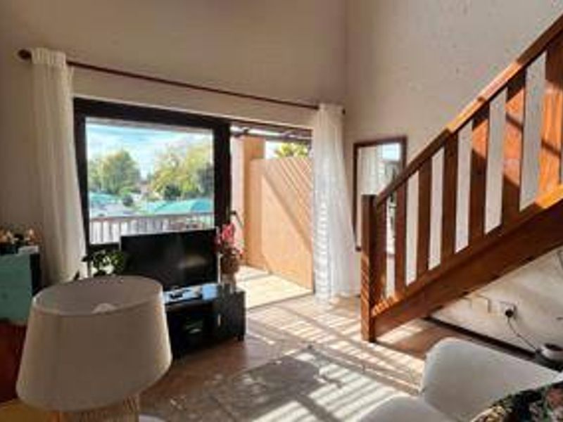 A bright living room featuring a wooden staircase, high ceilings, and sliding glass doors that open onto a private balcony.