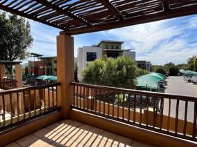 A covered balcony featuring a timber pergola and balustrade, offering an elevated view of the apartment complex and parking area.