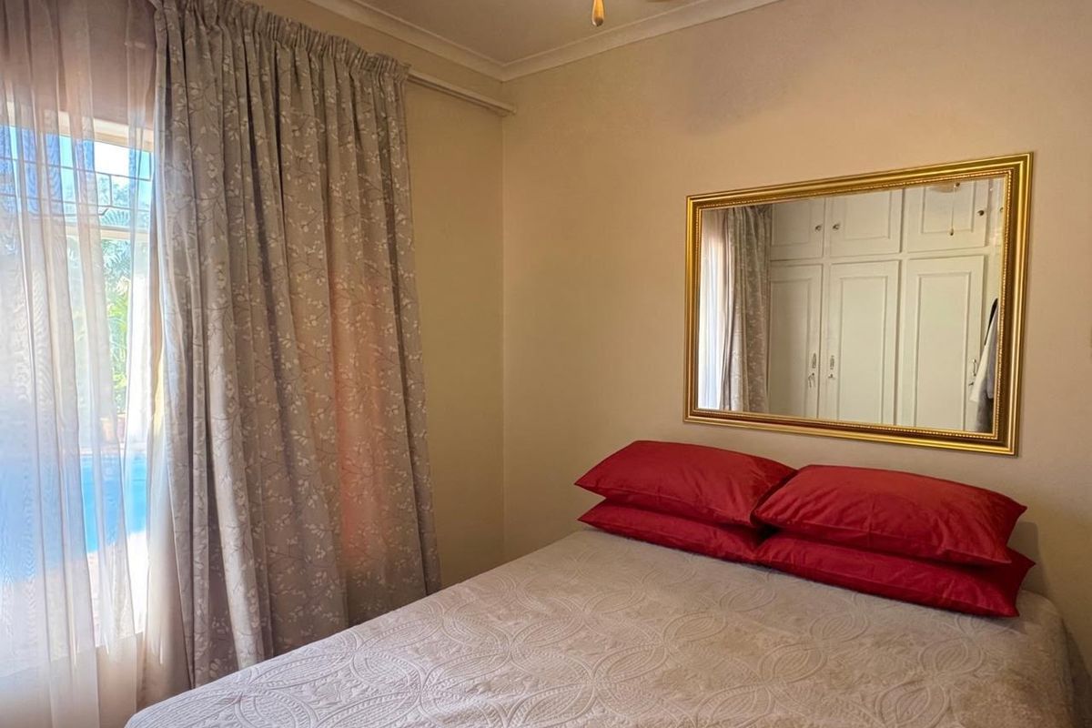 A cozy bedroom featuring built-in cupboards, a ceiling fan, and natural light filtering through curtains, offering a comfortable and functional living space.