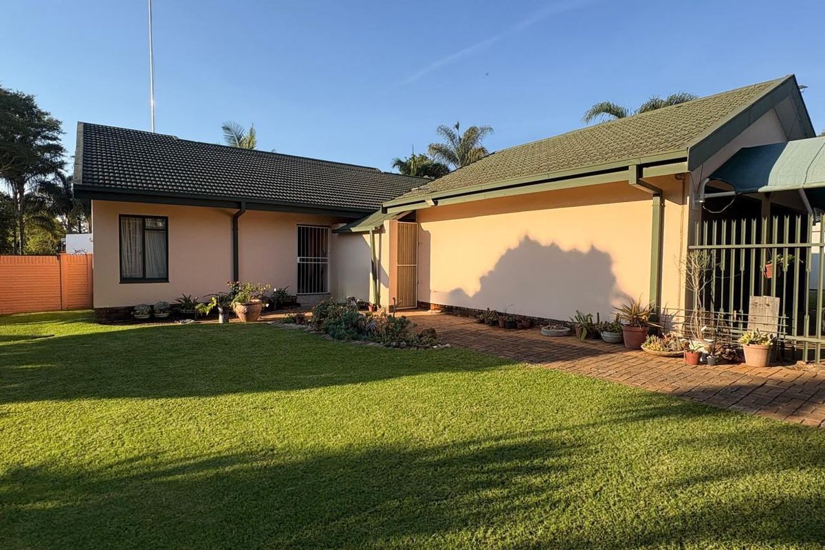 A view of the rear exterior of the house featuring a well-maintained lawn, brick paved pathway, and secure metal fencing.