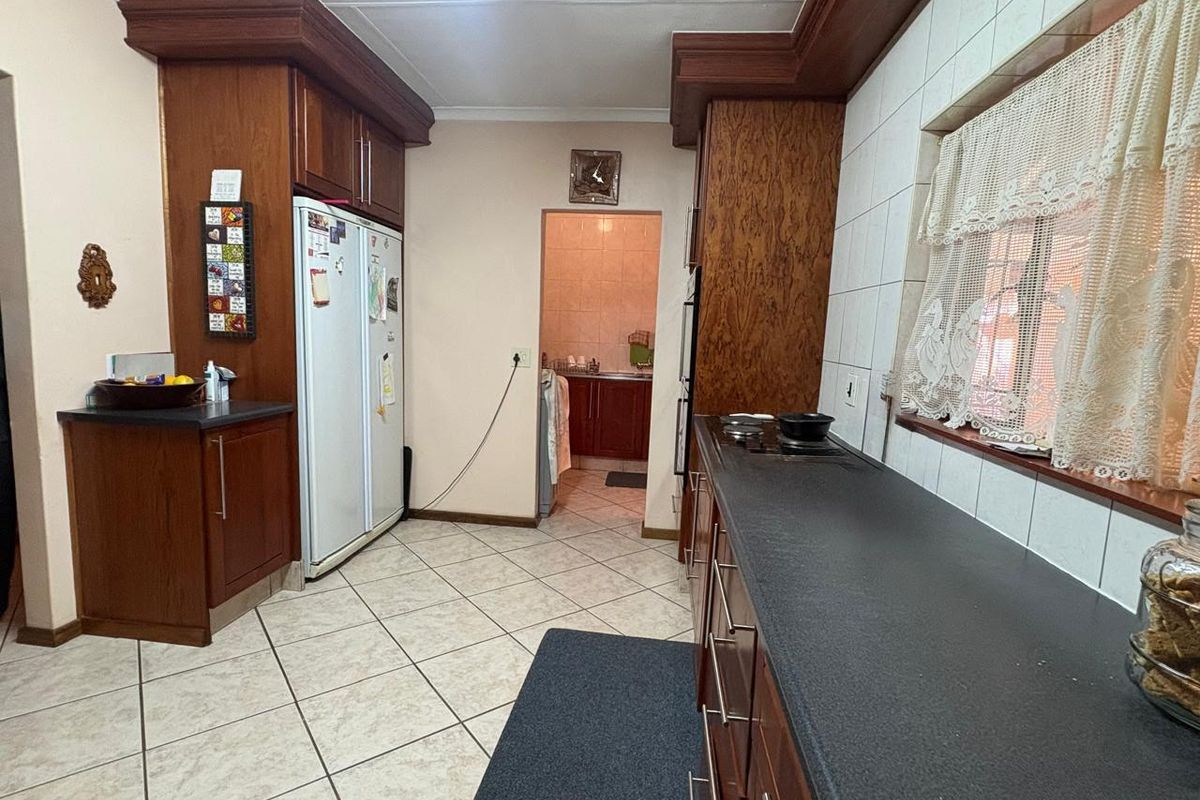A functional kitchen featuring dark wood cabinetry, laminate countertops, and tiled flooring, with an adjacent scullery area visible through the doorway.