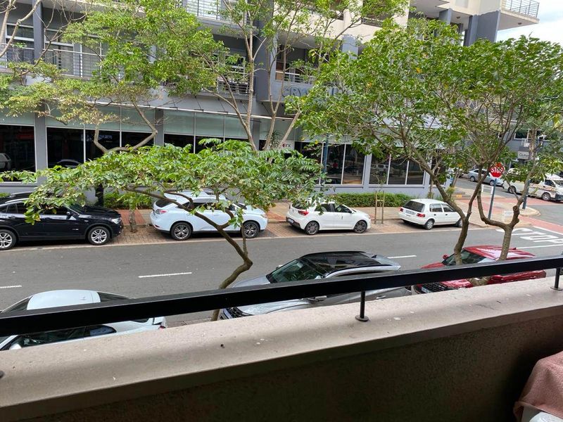 A street-level view looking out from a balcony towards the surrounding urban neighborhood and parked vehicles.