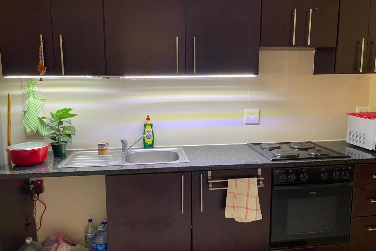A functional kitchen featuring dark wood cabinetry, a stainless steel sink, integrated electric hob, and built-in oven with under-cabinet lighting.