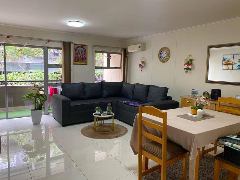 Bright open-plan living and dining area featuring large format floor tiles, a split-system air conditioner, and direct access to a private balcony.