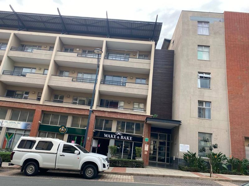 Front elevation of a multi-story apartment building featuring residential balconies above ground-floor commercial retail spaces and a secure main entrance.