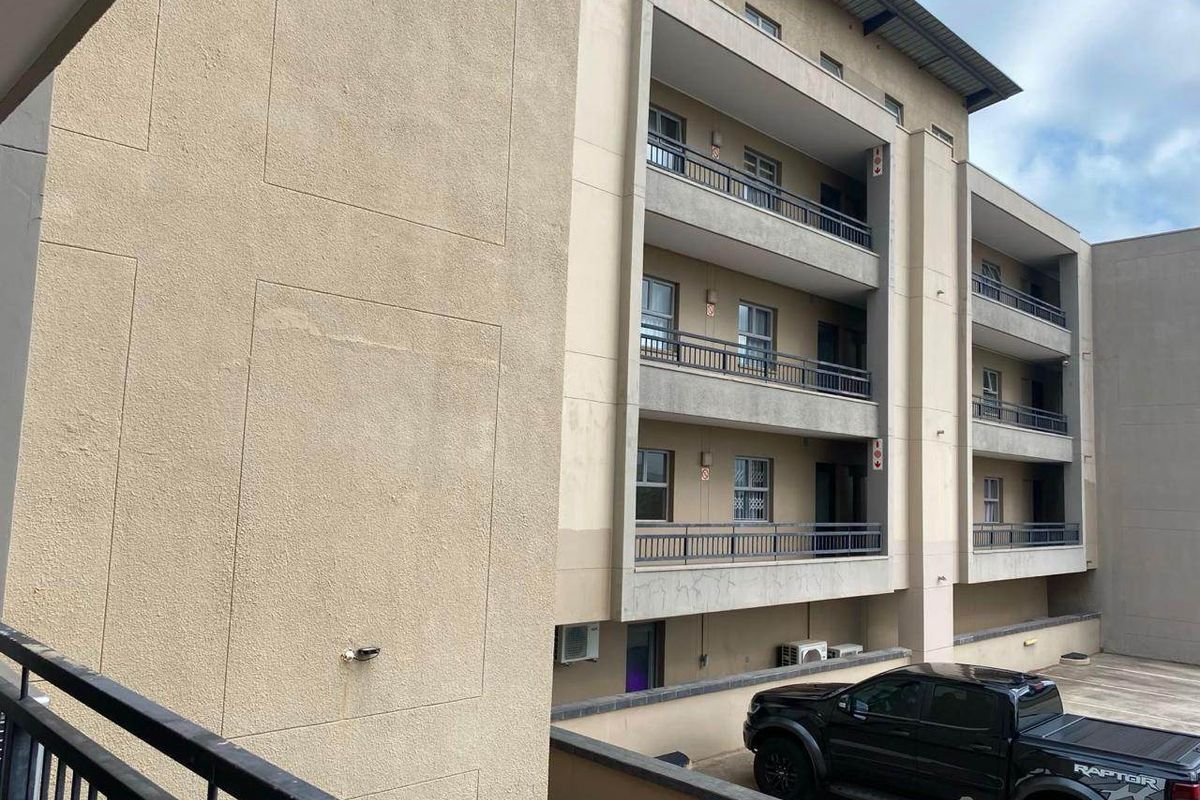 Exterior view of a multi-story apartment building featuring stacked balconies with metal railings and a textured stucco facade.