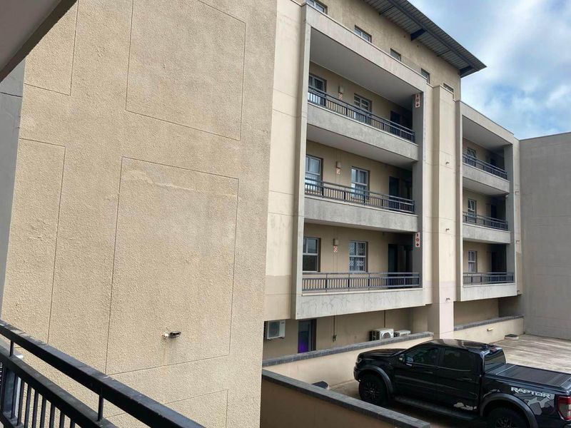 Exterior view of a multi-story apartment building featuring stacked balconies with metal railings and a textured stucco facade.
