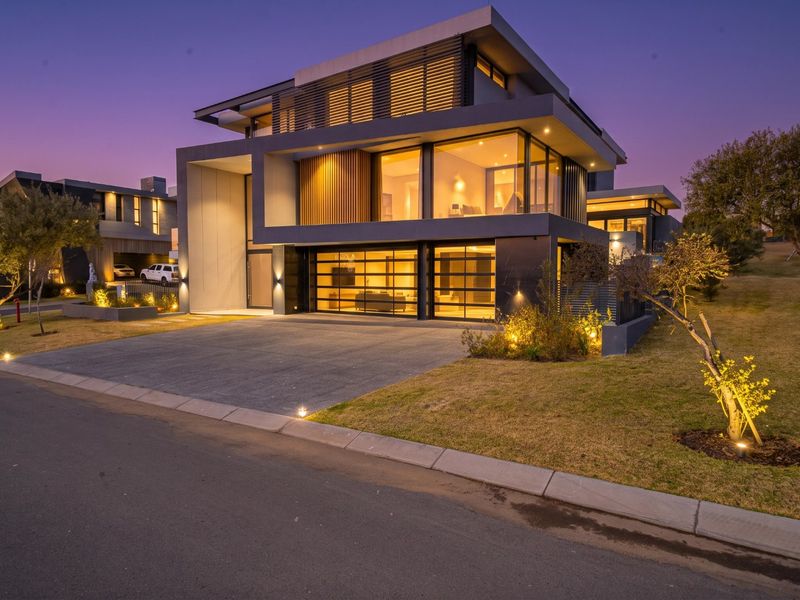 A stunning modern multi-story residence featuring a sleek facade, expansive glass windows, integrated garage doors, and professional exterior landscape lighting at dusk.