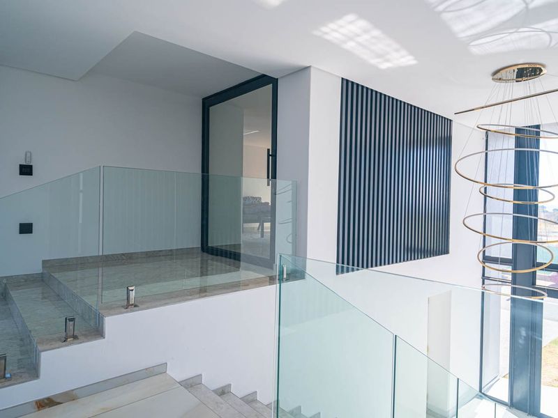 Modern entrance hallway featuring a glass balustrade, stone staircase, and decorative wall paneling with a contemporary chandelier.