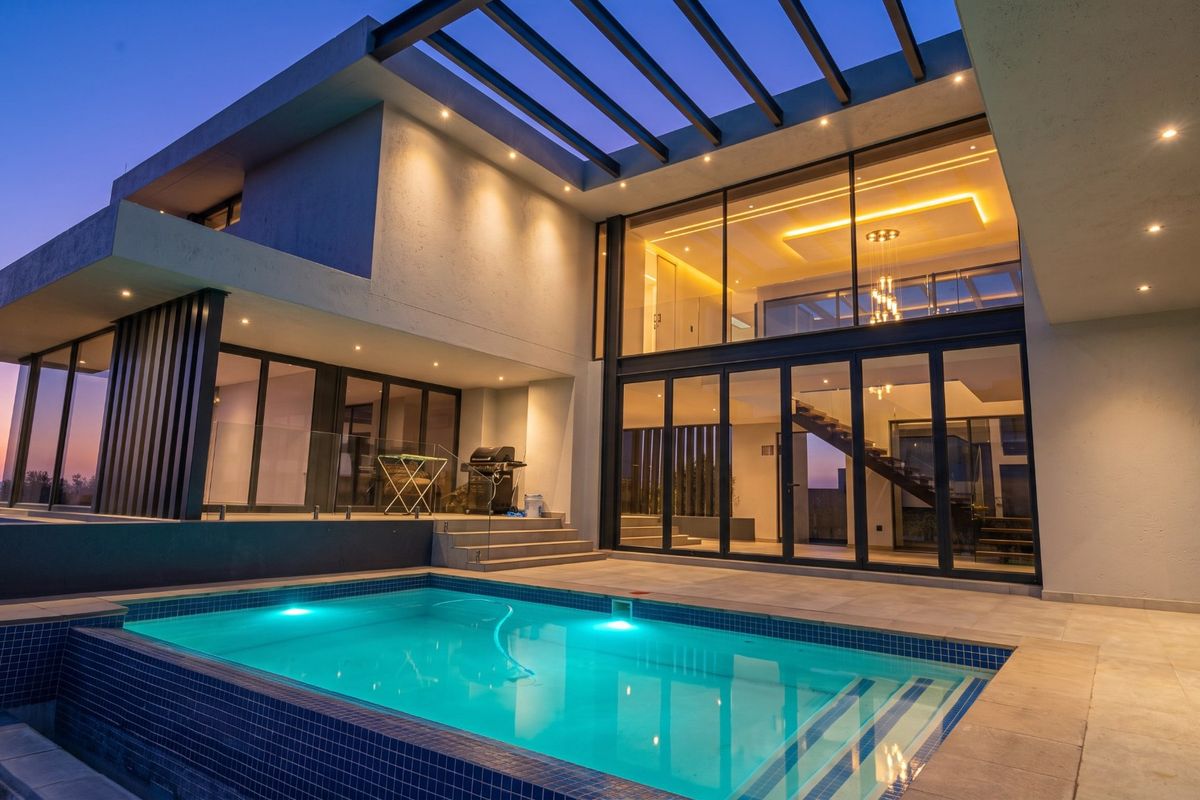 Modern luxury residence featuring a swimming pool, expansive glass facade, and a covered patio area, perfect for evening outdoor entertaining.