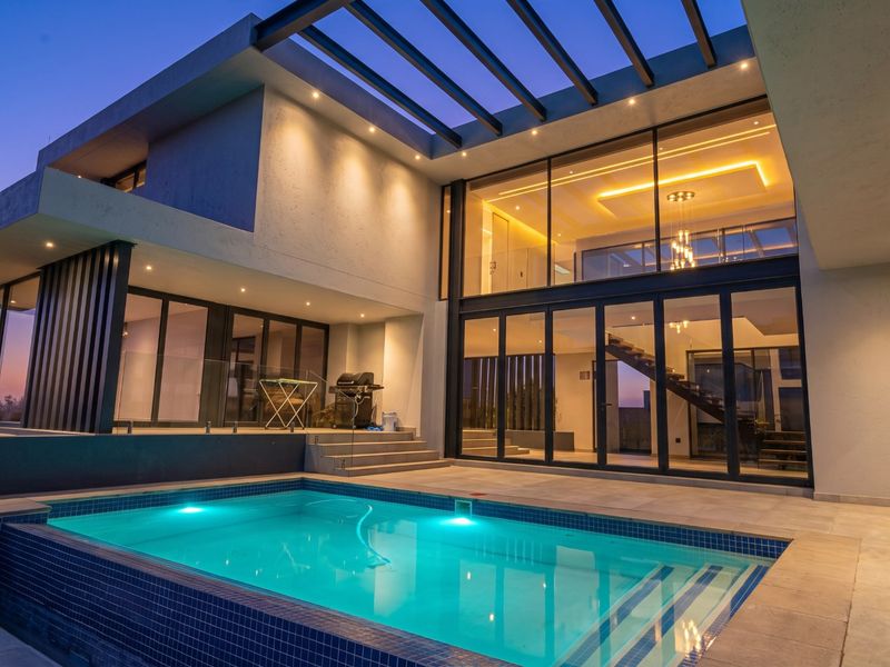 Modern luxury residence featuring a swimming pool, expansive glass facade, and a covered patio area, perfect for evening outdoor entertaining.