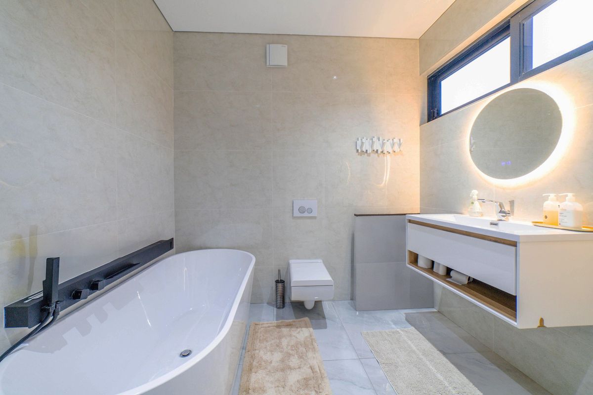 Modern bathroom featuring a sleek freestanding bathtub, wall-mounted toilet, and a floating vanity with a backlit mirror, finished with high-quality wall and floor tiling.
