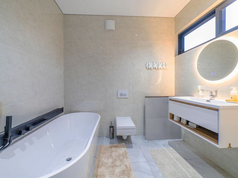 Modern bathroom featuring a sleek freestanding bathtub, wall-mounted toilet, and a floating vanity with a backlit mirror, finished with high-quality wall and floor tiling.