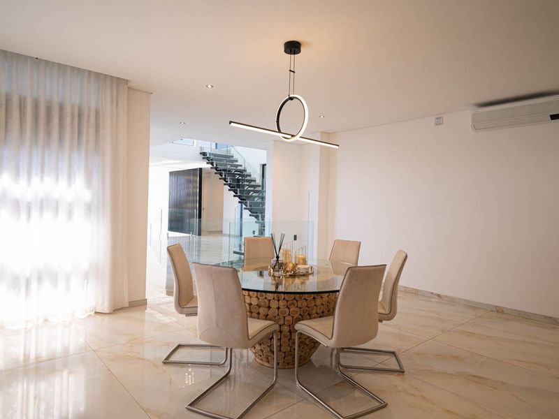 Elegant dining area featuring polished marble-look flooring, modern pendant lighting, and a view towards a contemporary staircase with glass balustrades.