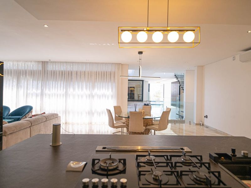 Spacious open-plan living and dining area featuring a modern kitchen island with gas hob, high-end finishes, and elegant pendant lighting throughout.