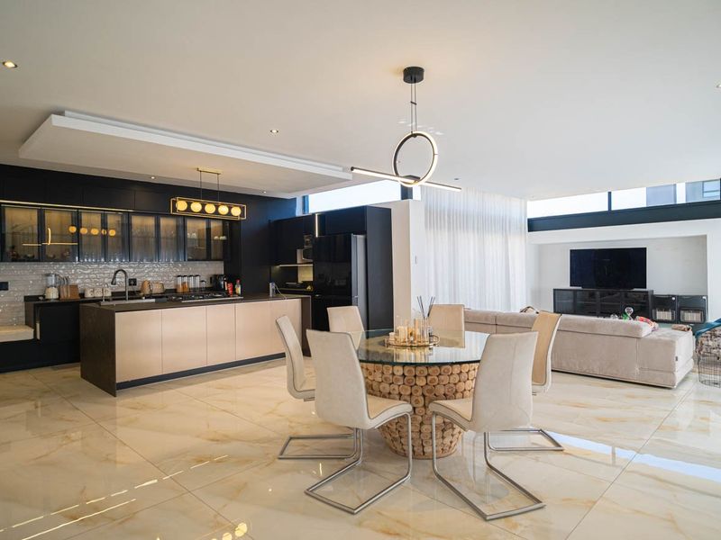 Modern open-plan living area featuring a sleek kitchen with island, high-end cabinetry, and polished marble-look flooring throughout the dining and lounge space.