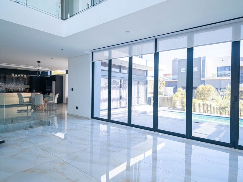 Spacious open-plan living area featuring high-gloss marble-look tiles, floor-to-ceiling glass doors opening to the pool area, and a modern glass staircase balustrade.