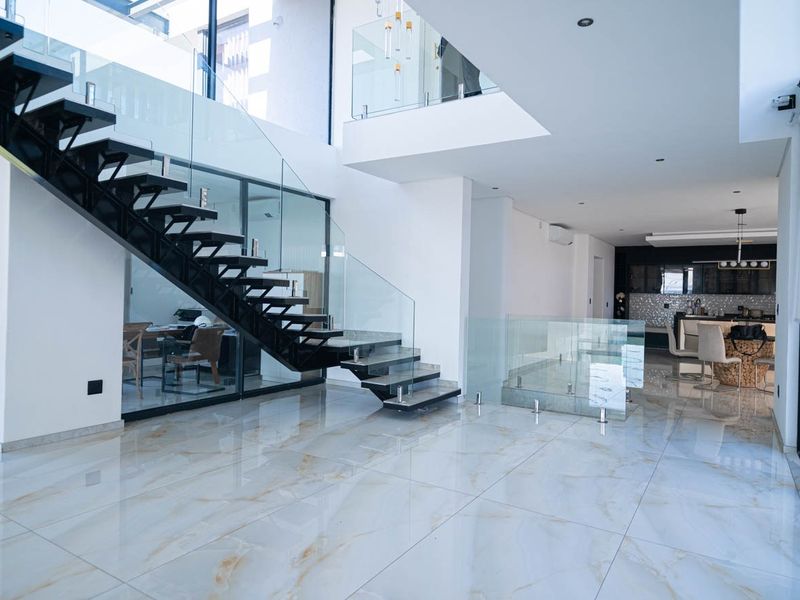 Spacious open-plan living area featuring a striking floating staircase with glass balustrades, high ceilings, and premium marble-look floor tiles.
