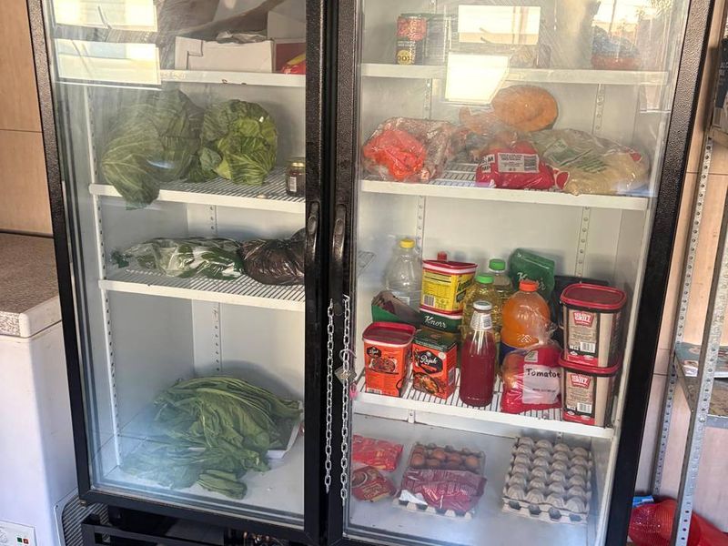 A commercial-grade double glass-door refrigerator unit positioned in a tiled kitchen area, used for cold storage of food supplies.