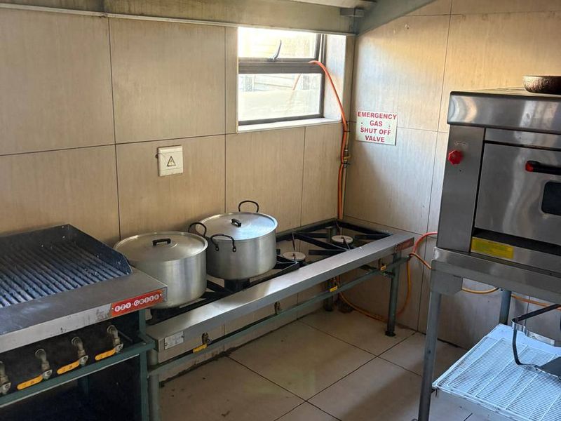 Commercial kitchen area featuring a stainless steel extractor hood, gas cooking station, and commercial oven with tiled finishes and safety gas shut-off valve.