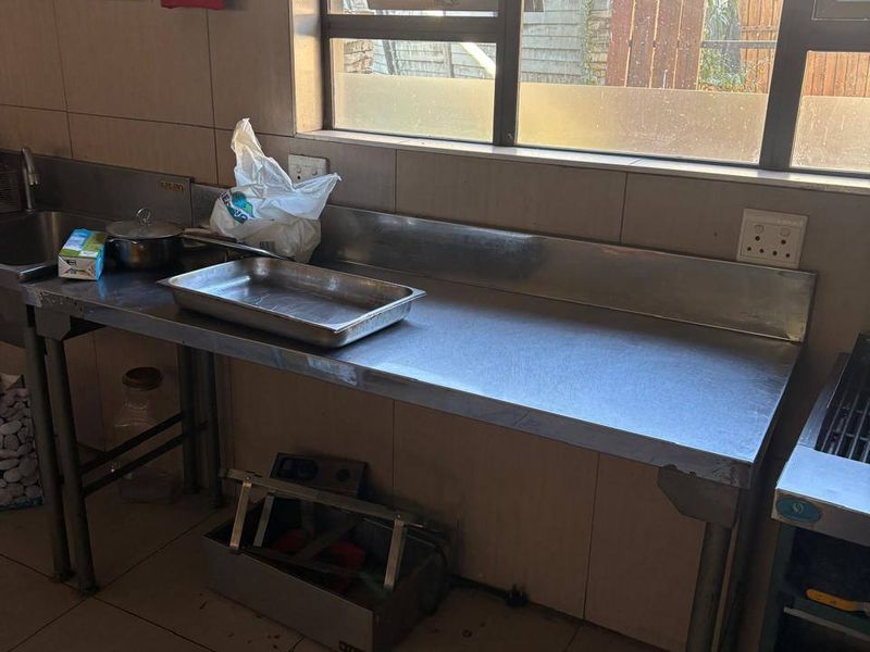 Commercial kitchen prep area featuring stainless steel work surfaces, integrated sink, tiled splashbacks, and functional window for natural light.
