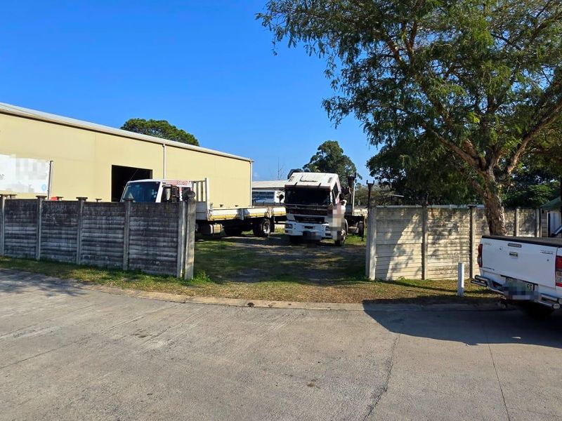 Front view of a vacant industrial plot featuring a precast concrete boundary wall and access to a warehouse structure.