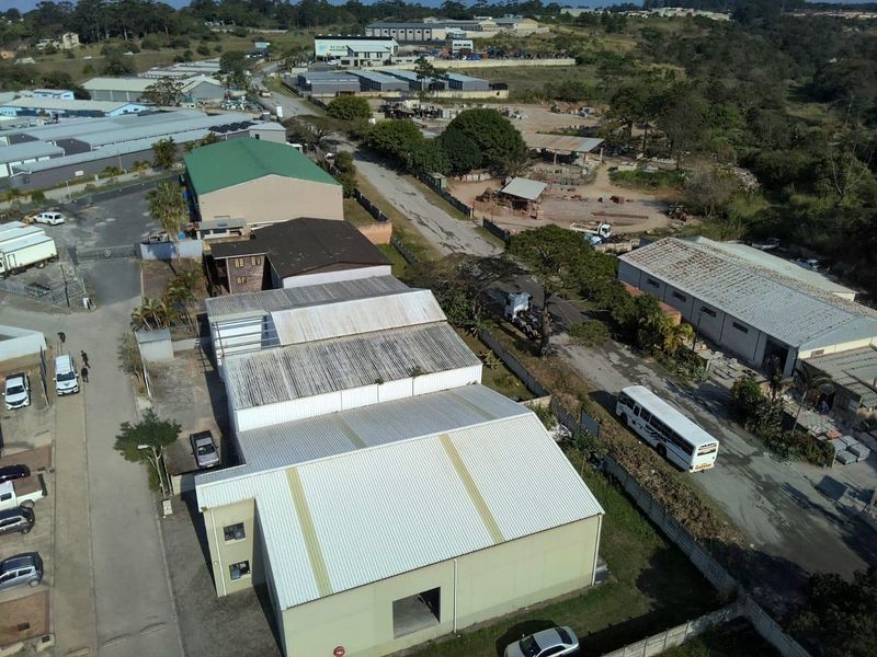 Aerial view of an industrial warehouse property featuring metal roofing and surrounding paved access roads within a commercial development area.