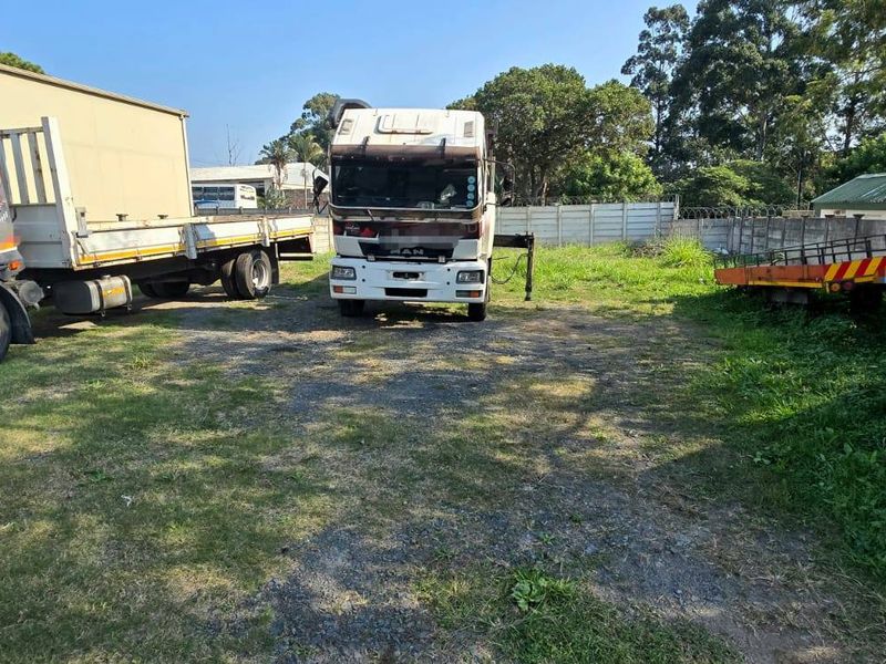 A vacant residential land plot featuring a gravel surface, enclosed by precast concrete walling and security fencing.