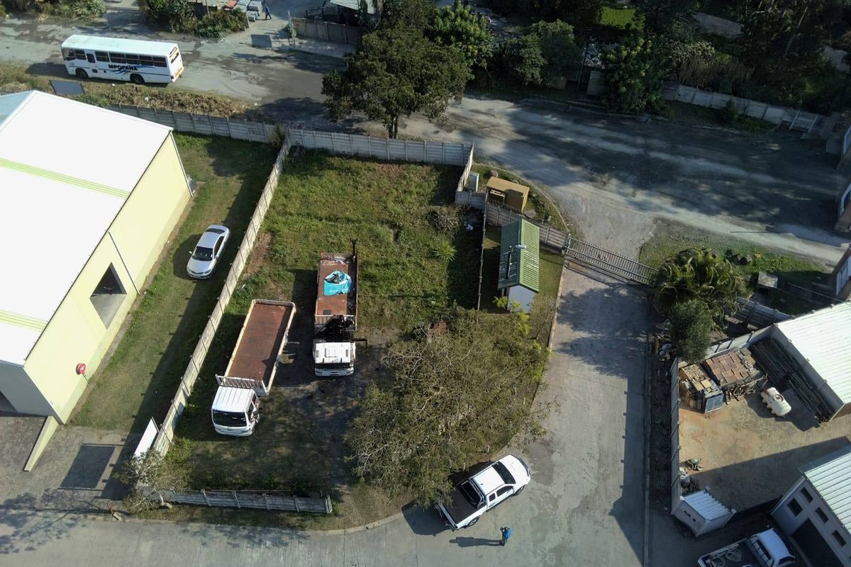Aerial view of a vacant residential plot featuring a perimeter boundary wall, gated access, and a small utility shed on site.