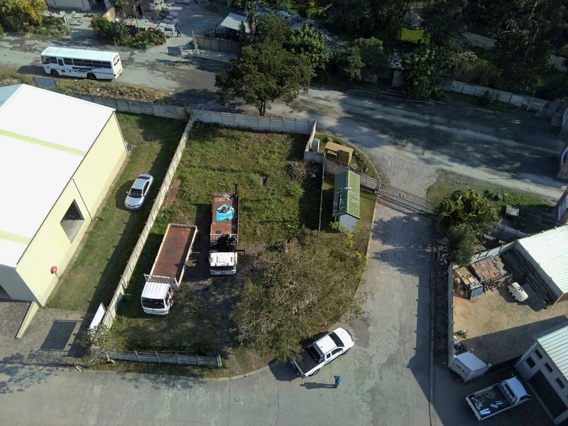 Aerial view of a vacant residential plot featuring a perimeter boundary wall, gated access, and a small utility shed on site.
