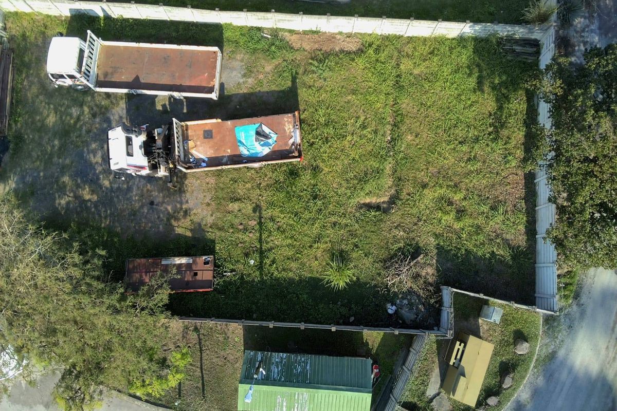 Aerial view of a vacant residential plot featuring perimeter fencing and overgrown grass, currently used for storage.