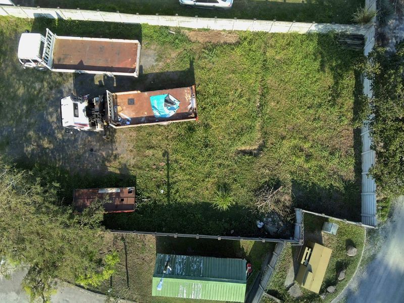Aerial view of a vacant residential plot featuring perimeter fencing and overgrown grass, currently used for storage.
