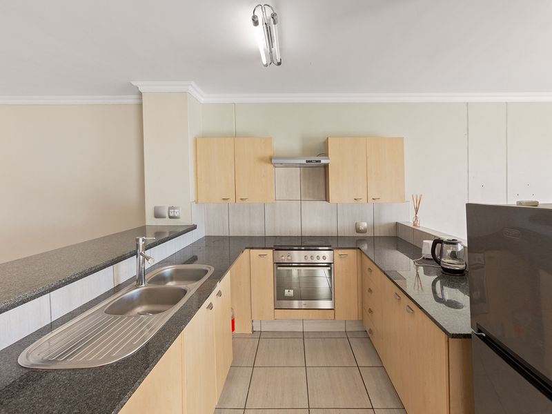 A functional kitchen featuring granite countertops, stainless steel sink, built-in oven with hob, extractor fan, and ample laminate cabinetry.
