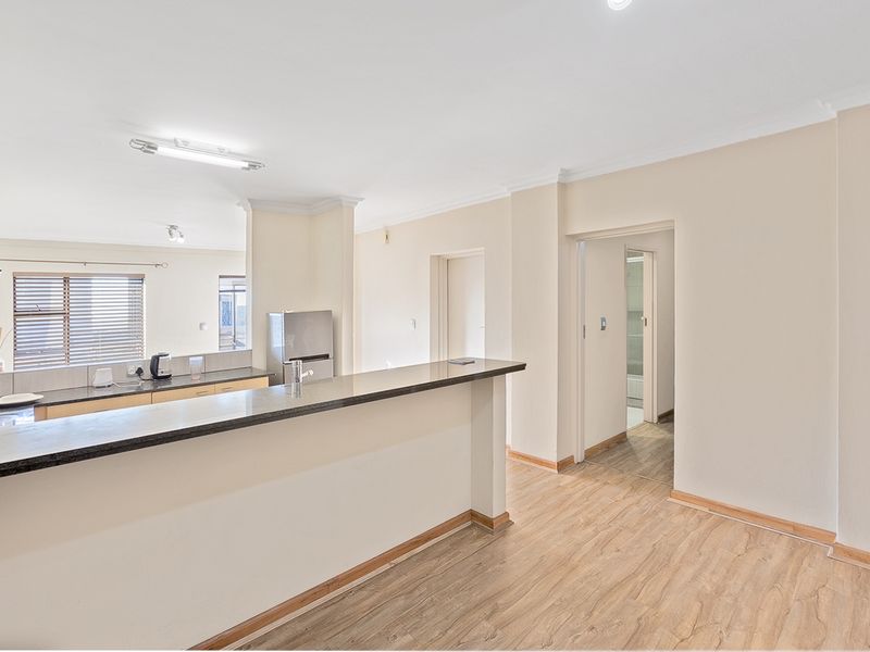 An open-plan living and kitchen area featuring laminate flooring, a granite breakfast bar, and neutral walls, offering a bright and functional layout.
