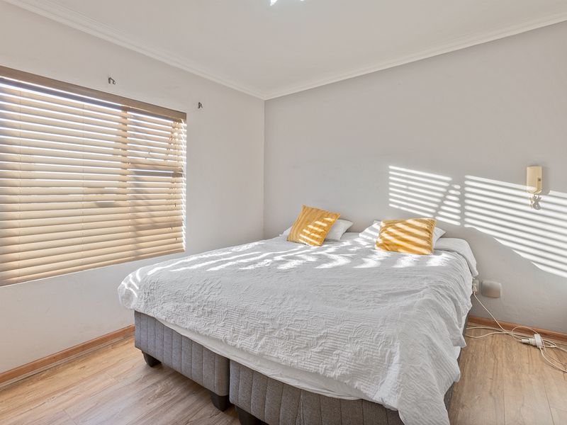 A well-lit bedroom featuring laminate flooring, coving, and venetian blinds, providing a comfortable and functional living space.